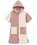 A short-sleeve hooded zip-up towel robe in a color-blocked design of dusty pink and cream, featuring two large front patch pockets, shown against a plain white background.